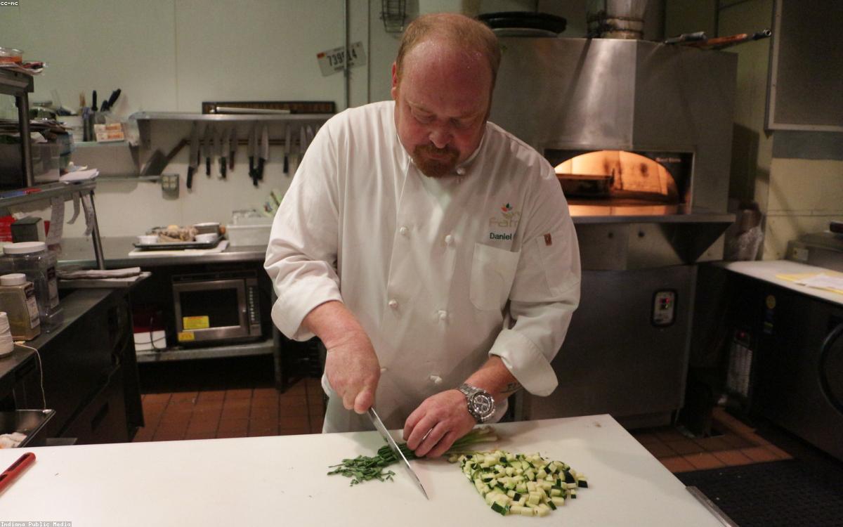 A chef knife resting on a wooden cutting board with fresh vegetables