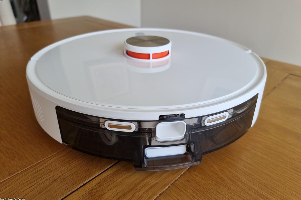 A robot vacuum cleaning a living room floor beside a sofa